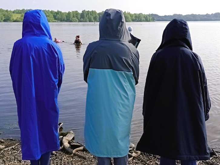 three people wearing a changing robe, looking out over the lake.